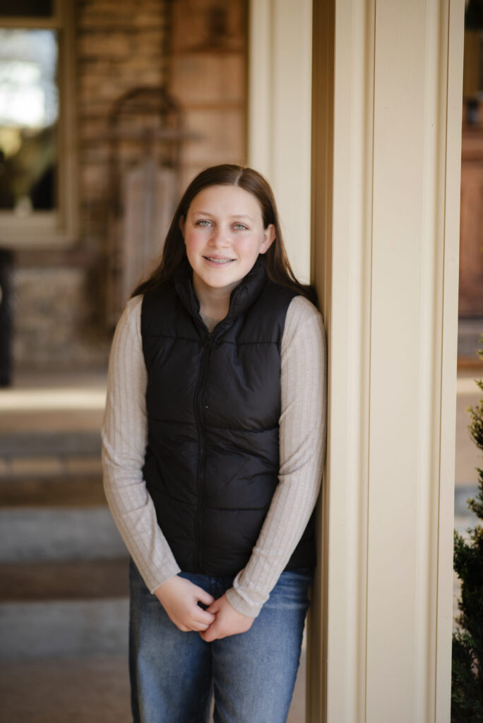 Young woman wearing black puffer vest photographed on porch during photo session with Henwood Studios.
