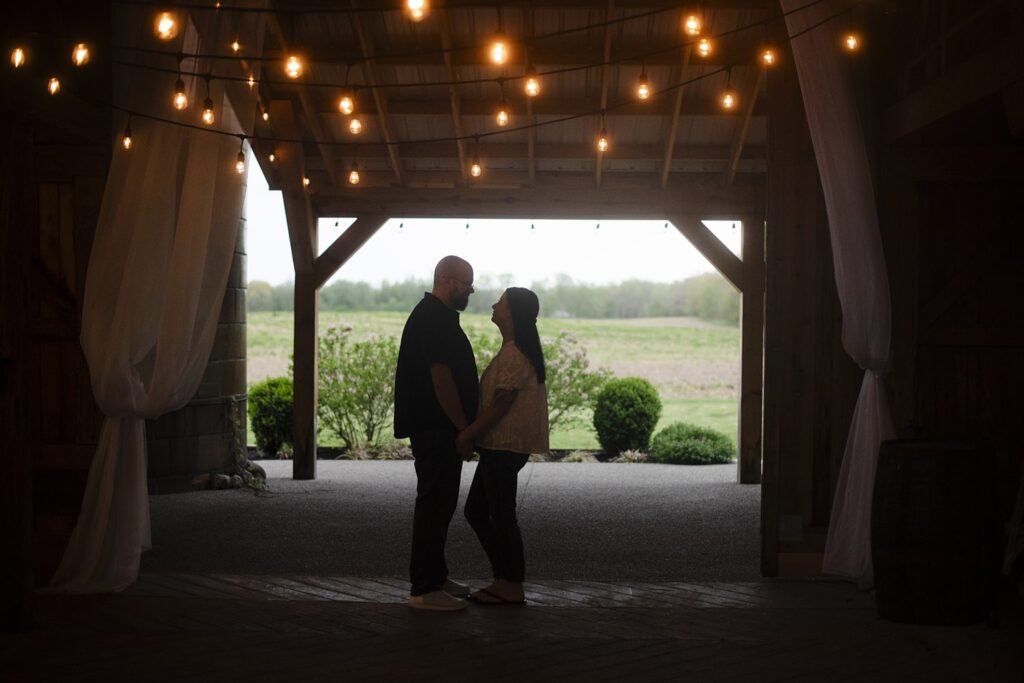 Couple looking loving at each other, holding hands under a string of lights.