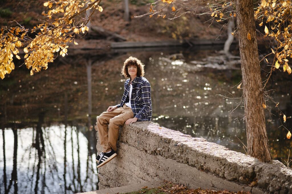 High school senior portrait of young man sitting on concrete blocks above a river.