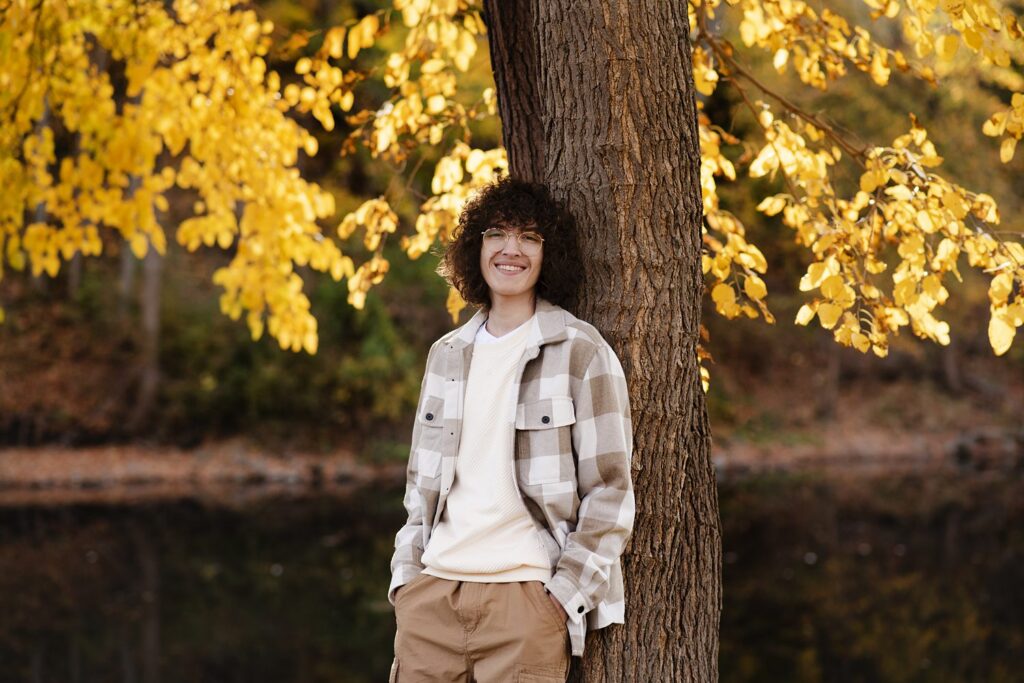 Young man confidently smiling standing against a tree during senior photo session.