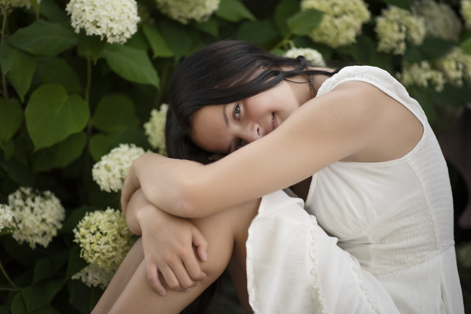 Close up senior portrait of young girl in a white dress photographed against white flowers.