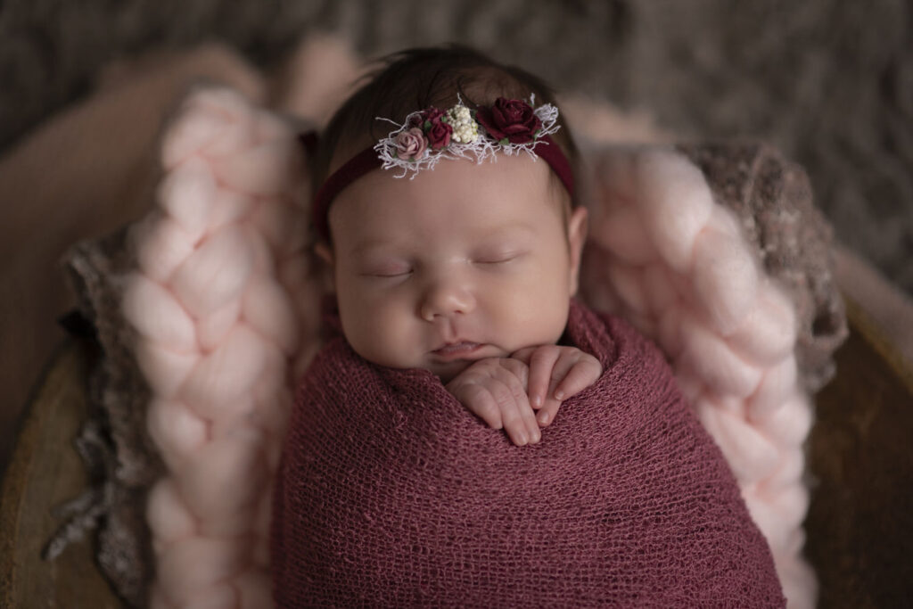 Adorable newborn photo of baby girl swaddled in a blanket during session with Henwood Studios.