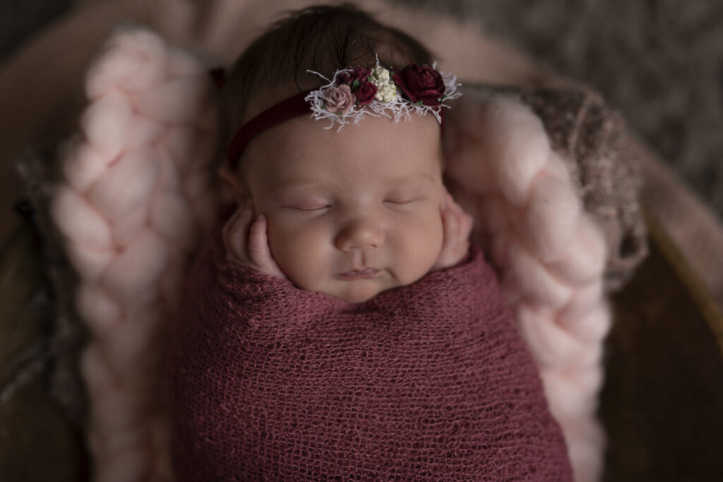 Close up photo of newborn wearing a rose headband gently touching her cheeks.