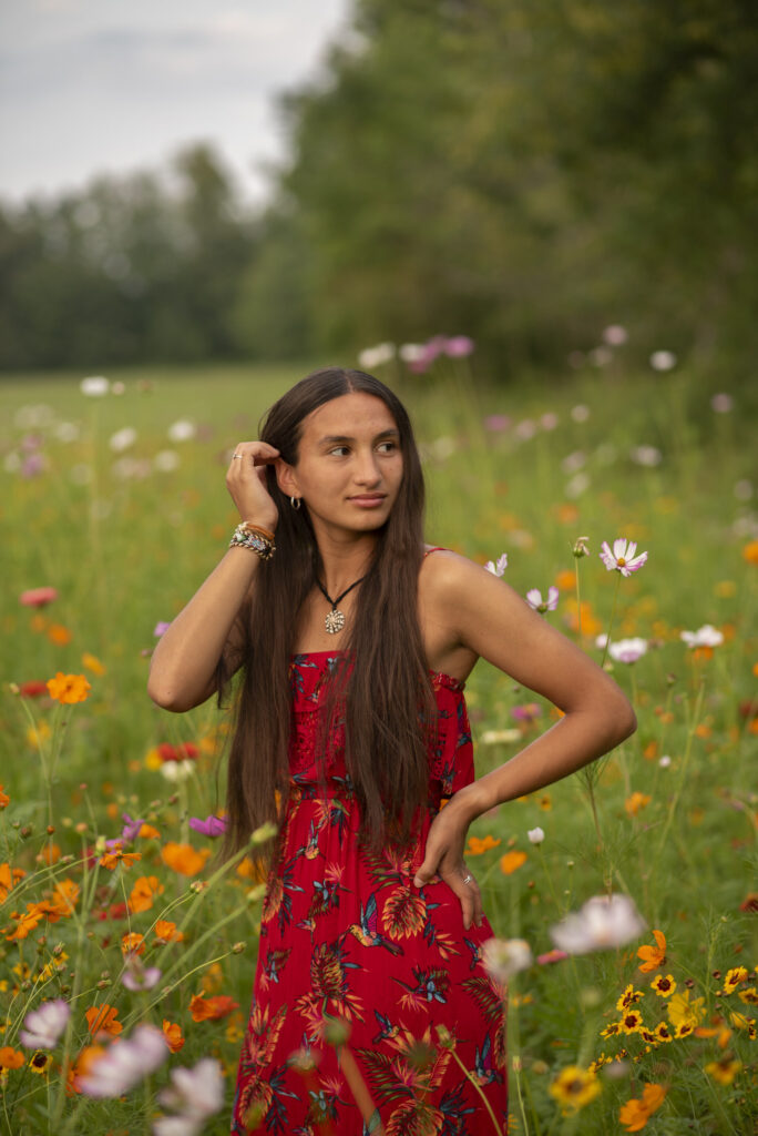 Confident high school senior wearing a red dress tucking her hair behind her ear among wildflowers.