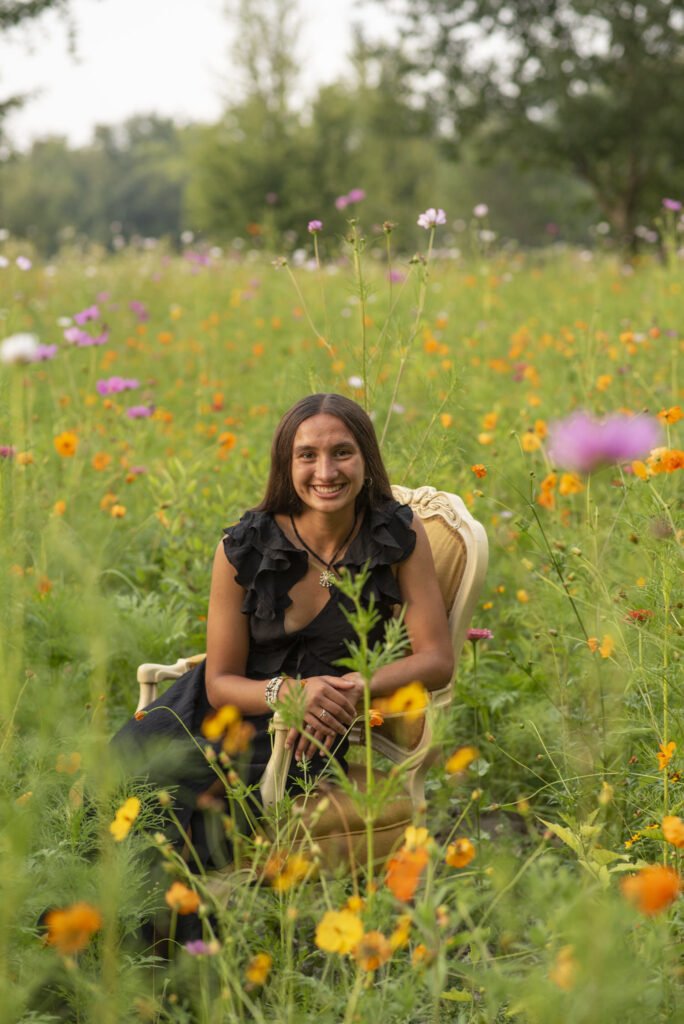 Classic senior portrait of girl sitting in an antique chair in a field of wildflowers.