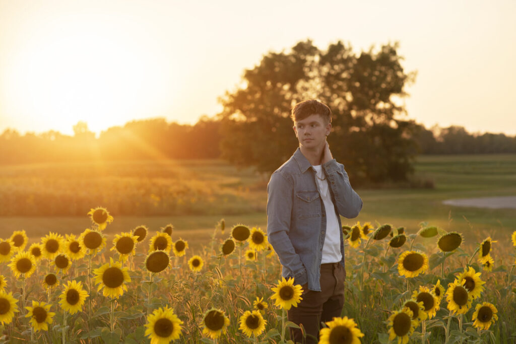 Portrait of high school senior standing in a sunflower field at sunset taken by Henwood Studios.