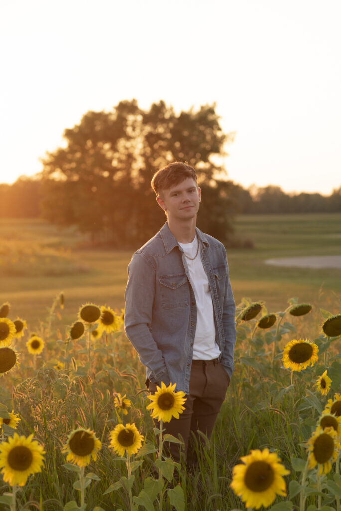 Portrait of high school senior with his hands in his pockets standing in a sunflower field.
