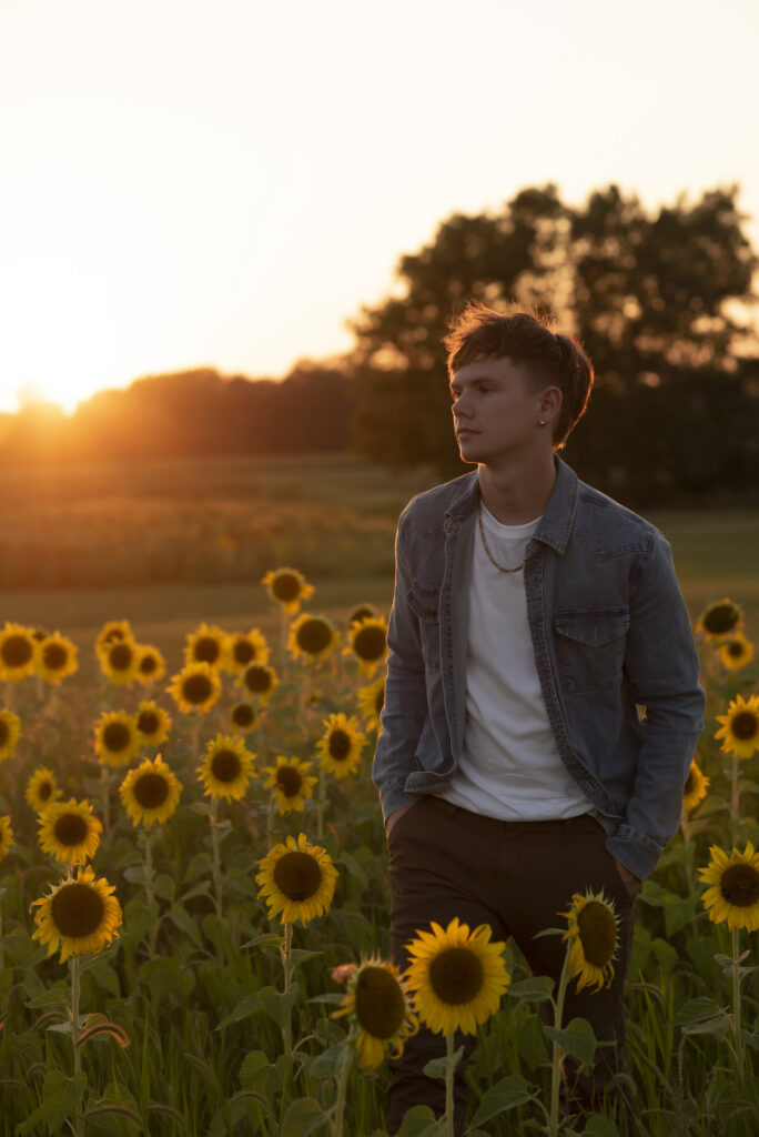 Dreamy portrait of young man in a sunflower field at dusk during his senior session with Henwood Studios.