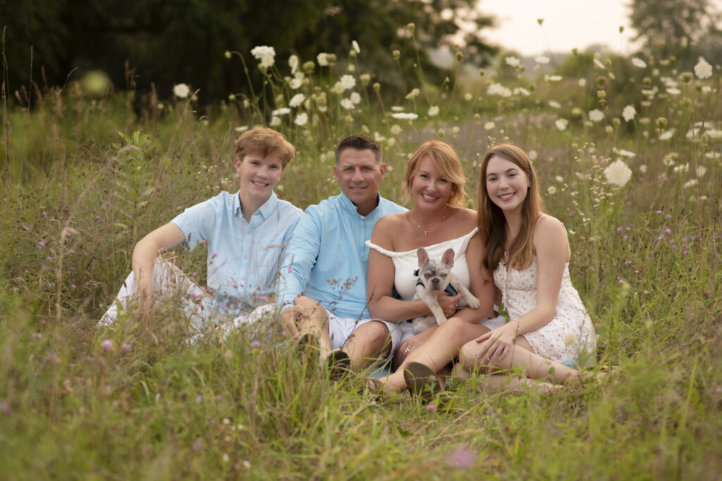 Group portrait of family of four and their dog sitting in a field.