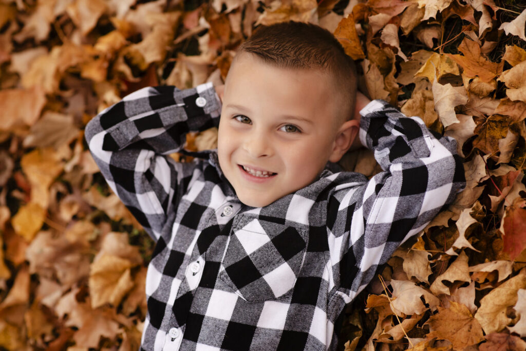 Close up portrait of little boy smiling at the camera surrounded by fall leaves.