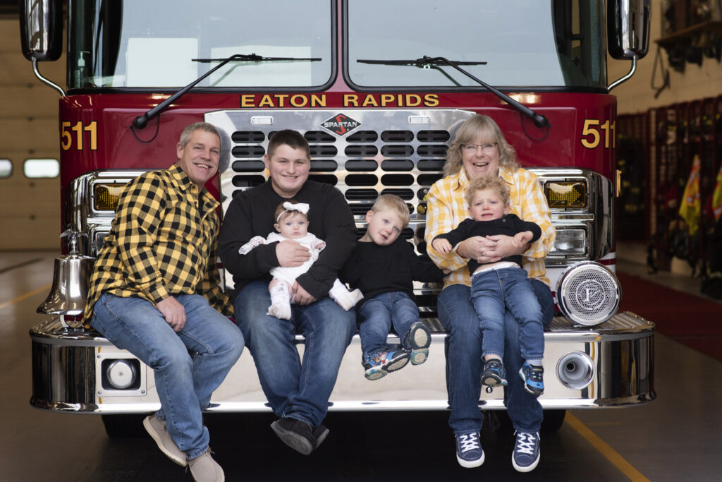 Grandma and Grandpa with their grandchildren seated atop the bumper of Eaton Rapids Fire truck.