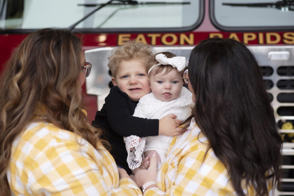 Family cuddled up in front of Eaton Rapids fire truck hugging during session with Henwood Studios.