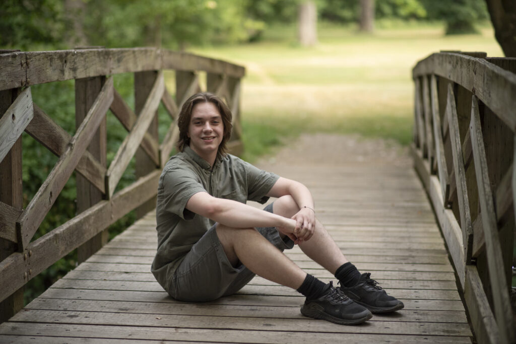 Classic senior portrait of young man sitting on wooden bridge.