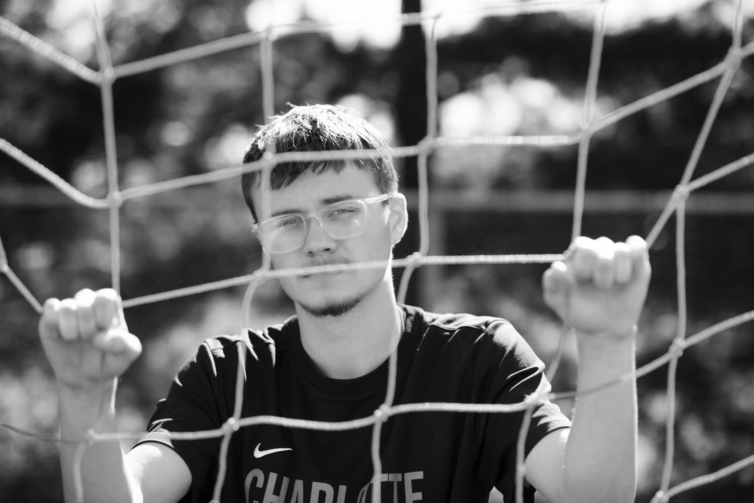 Black and white close up of high school senior photographed through a soccer net.