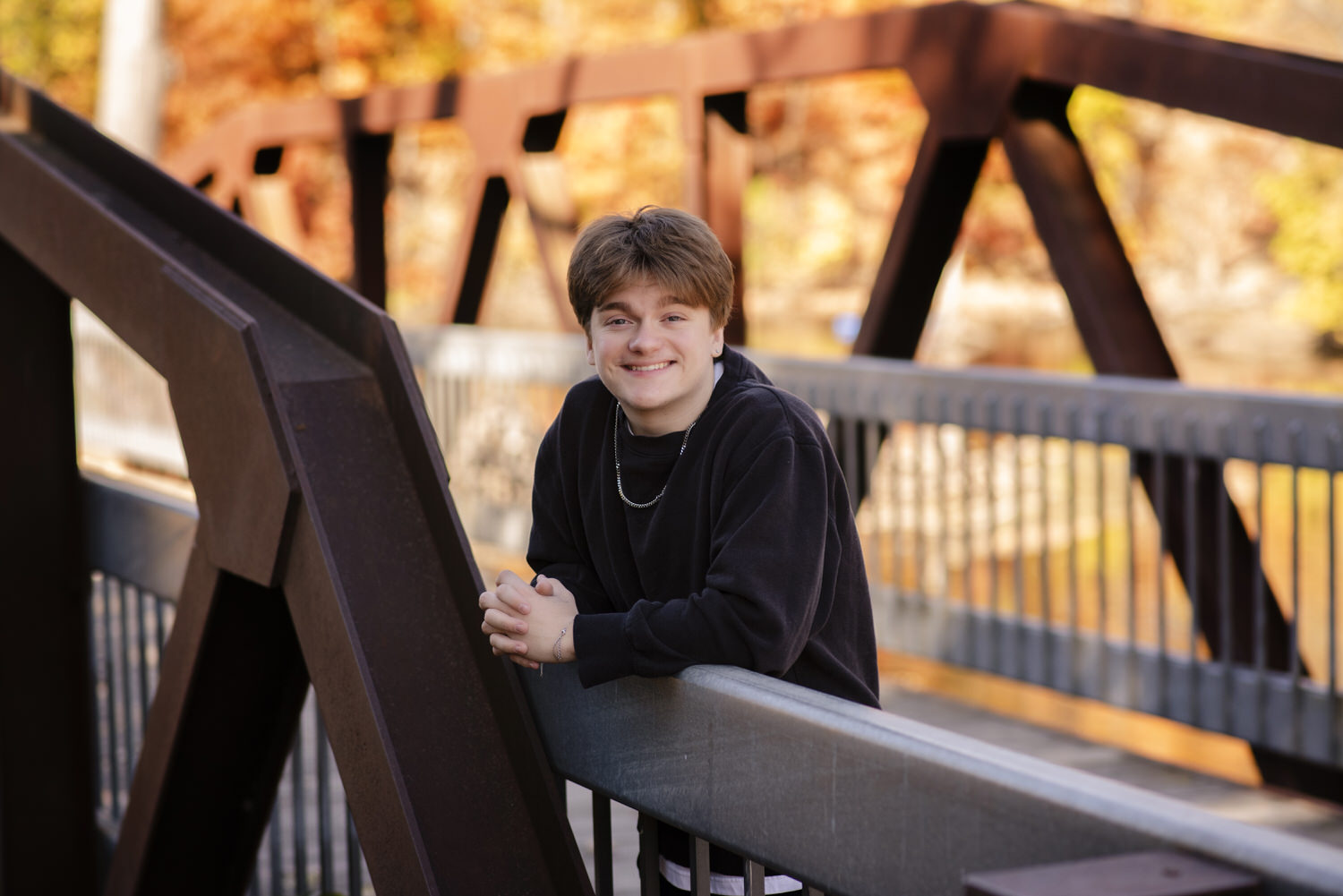 High school senior portrait of young man leaning on a bridge.