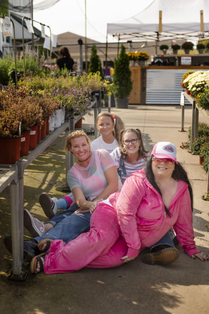 Four besties smile at the camera while seated on the ground in the garden section of Horrocks in Lansing, Michigan.