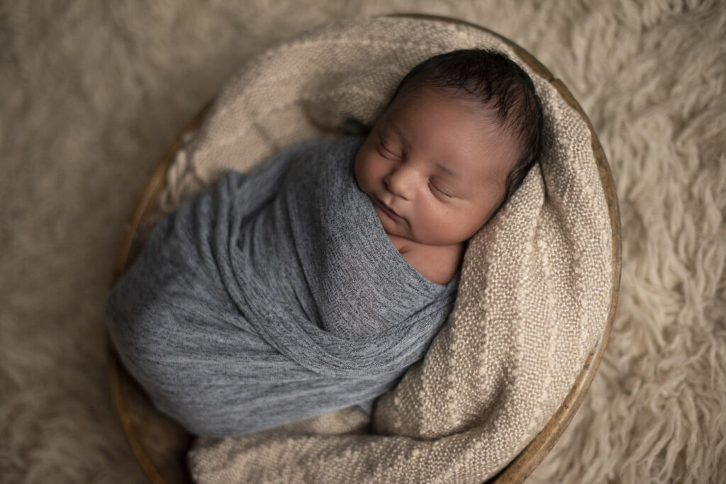 Precious newborn boy nestled in a cozy basket at Henwood Studios.