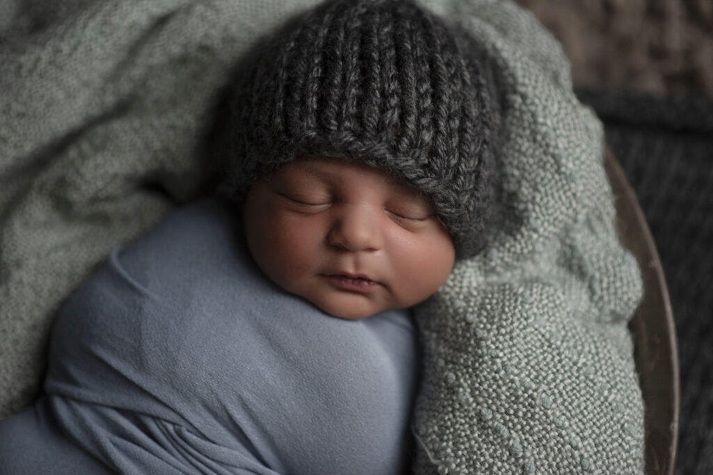 Newborn boy wearing knitted cap lying in basket.