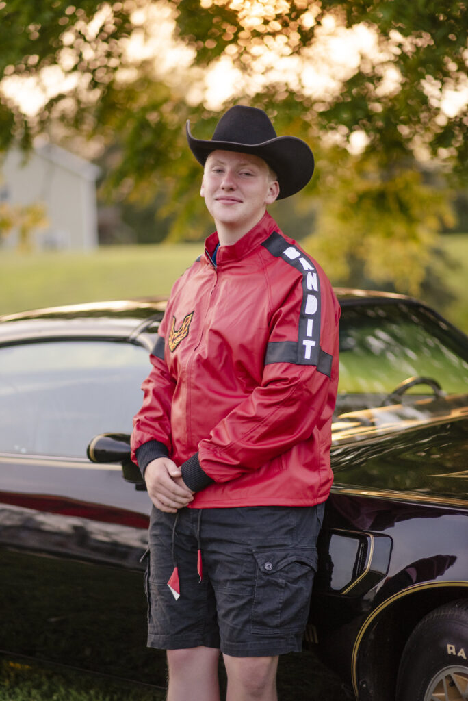 Senior portrait of young man wearing cowboy hat leaning against classic Pontiac.