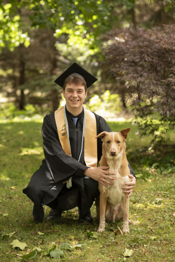 Senior on graduation day wearing cap and gown photographed with his dog.