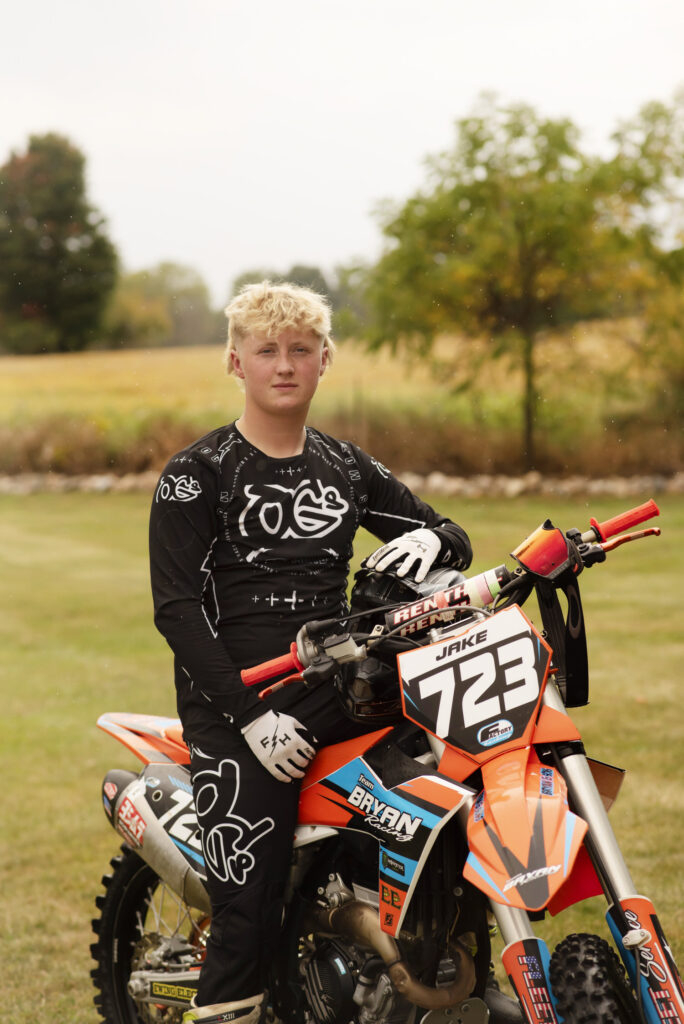 Close up portrait of high school senior sitting on his dirt bike wearing motocross gear taken by Henwood Studios.